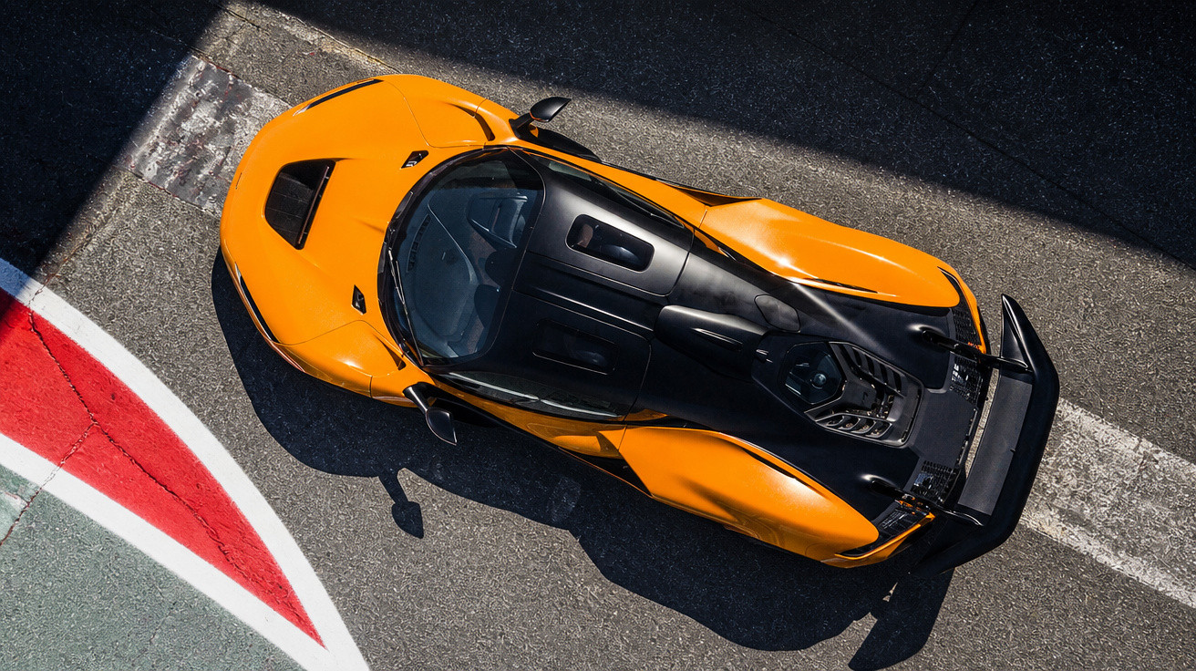 Top-down view of an orange and black sports car on a race track near a red and white curb.