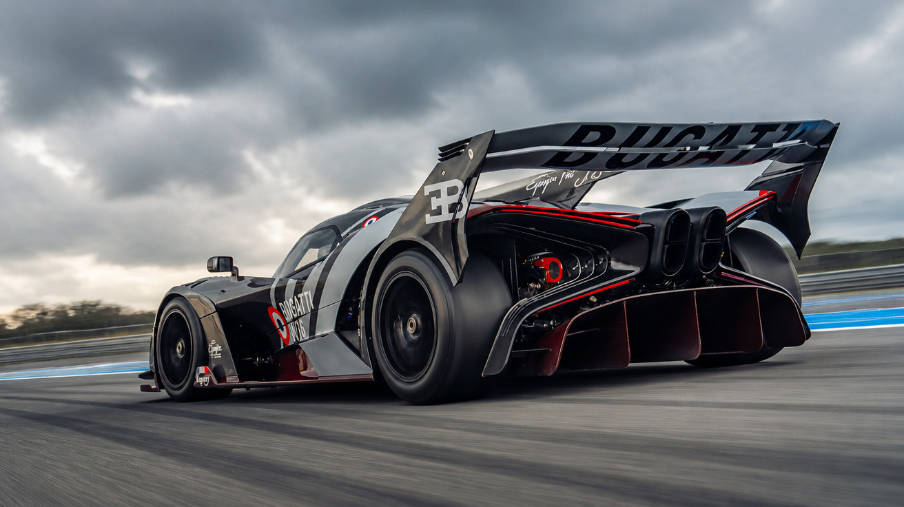 Black and red Bugatti race car speeding on track under a cloudy sky from rear angle.