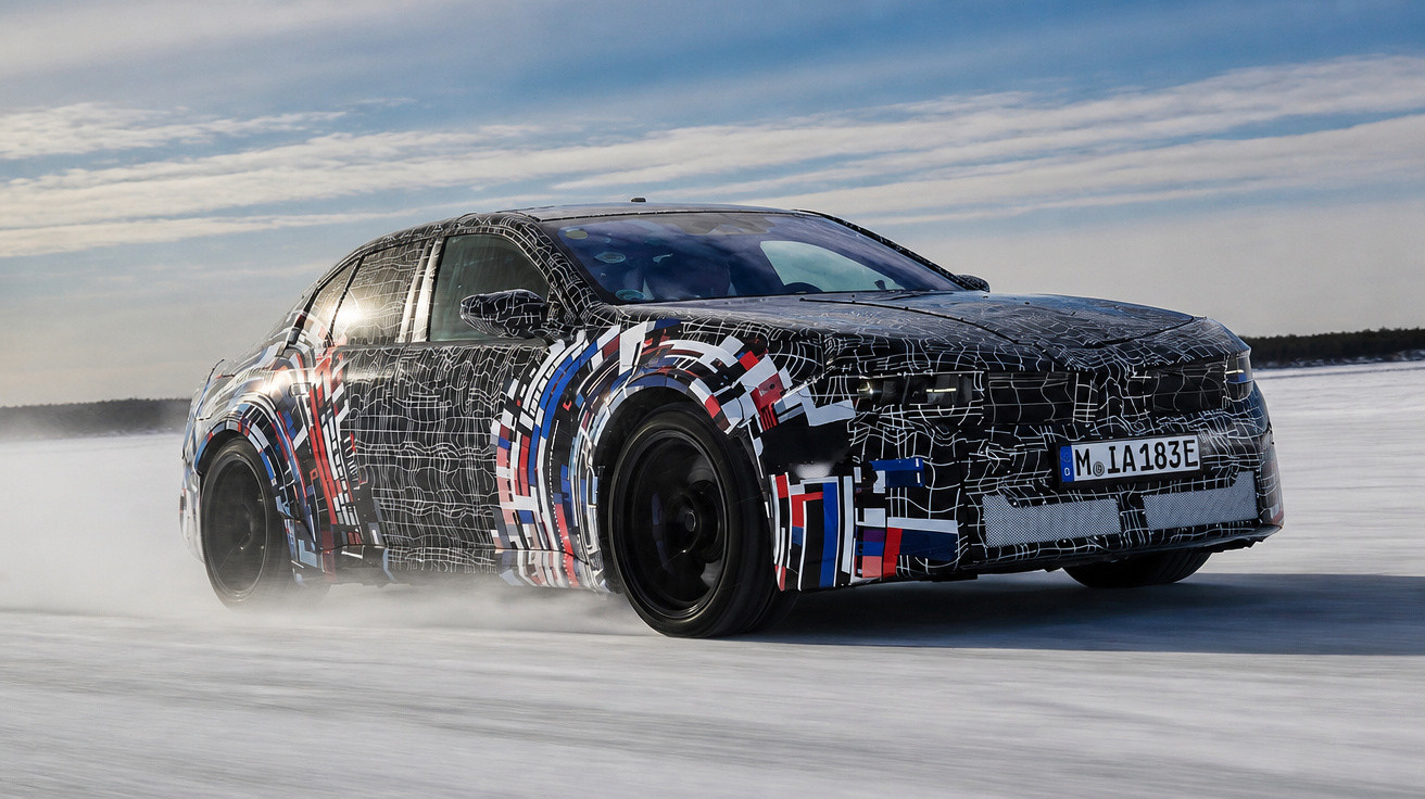 Black and patterned car driving fast on an icy road under a cloudy sky.