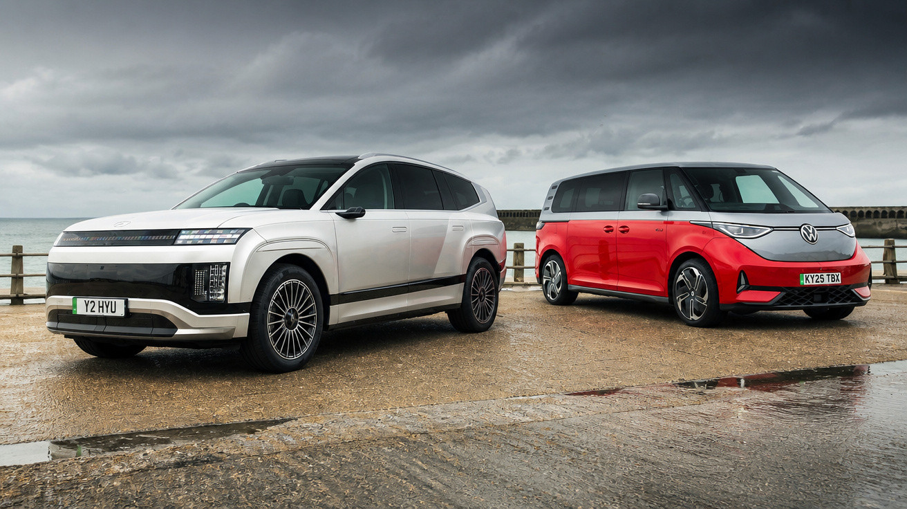 Two modern electric vehicles, a white SUV and a red MPV, parked on a wet pier under cloudy skies.