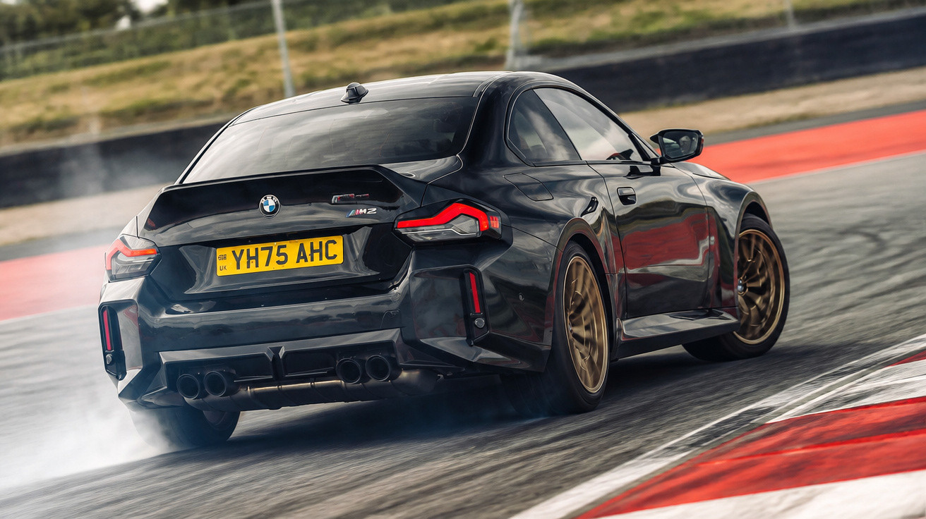Black BMW M2 drifting on a race track, rear view showing UK licence plate YH75 AHC.